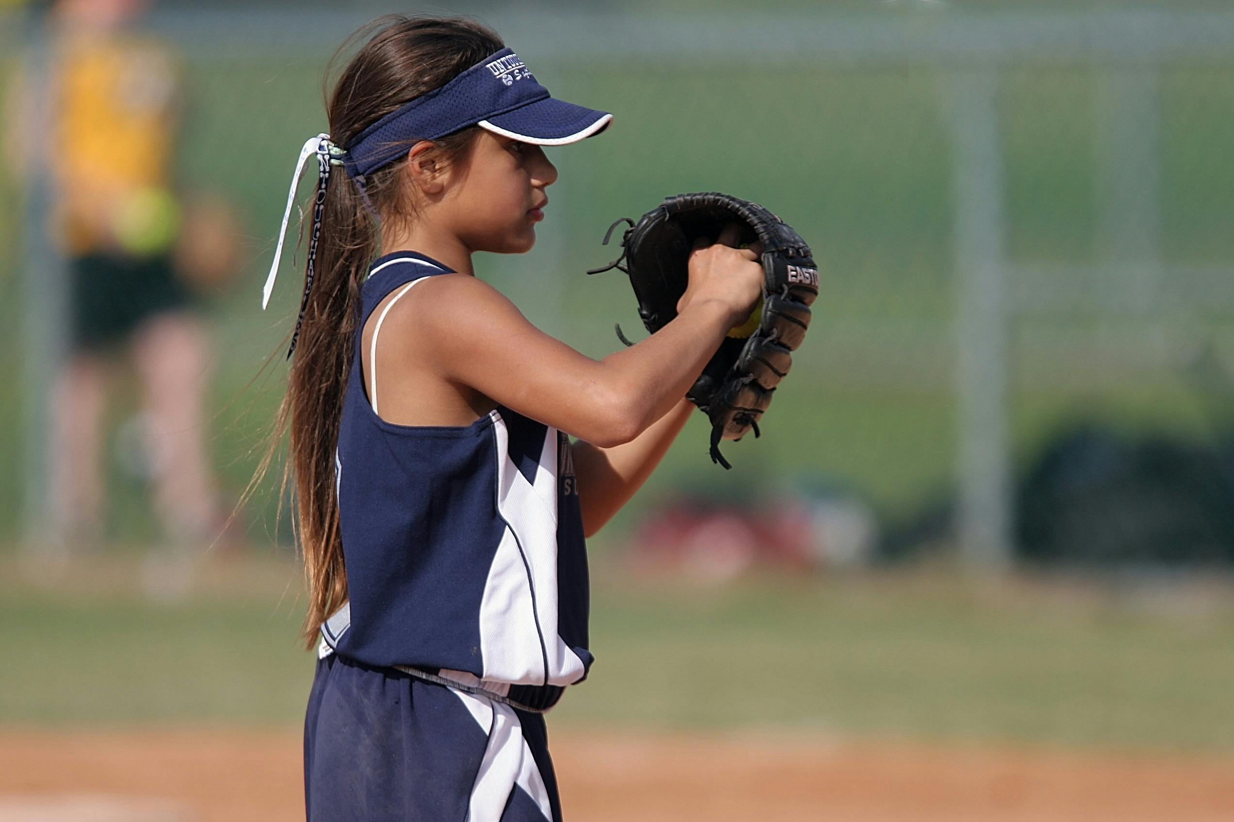 Young girl playing softball, preparing to pitch on a sunny day in the park.